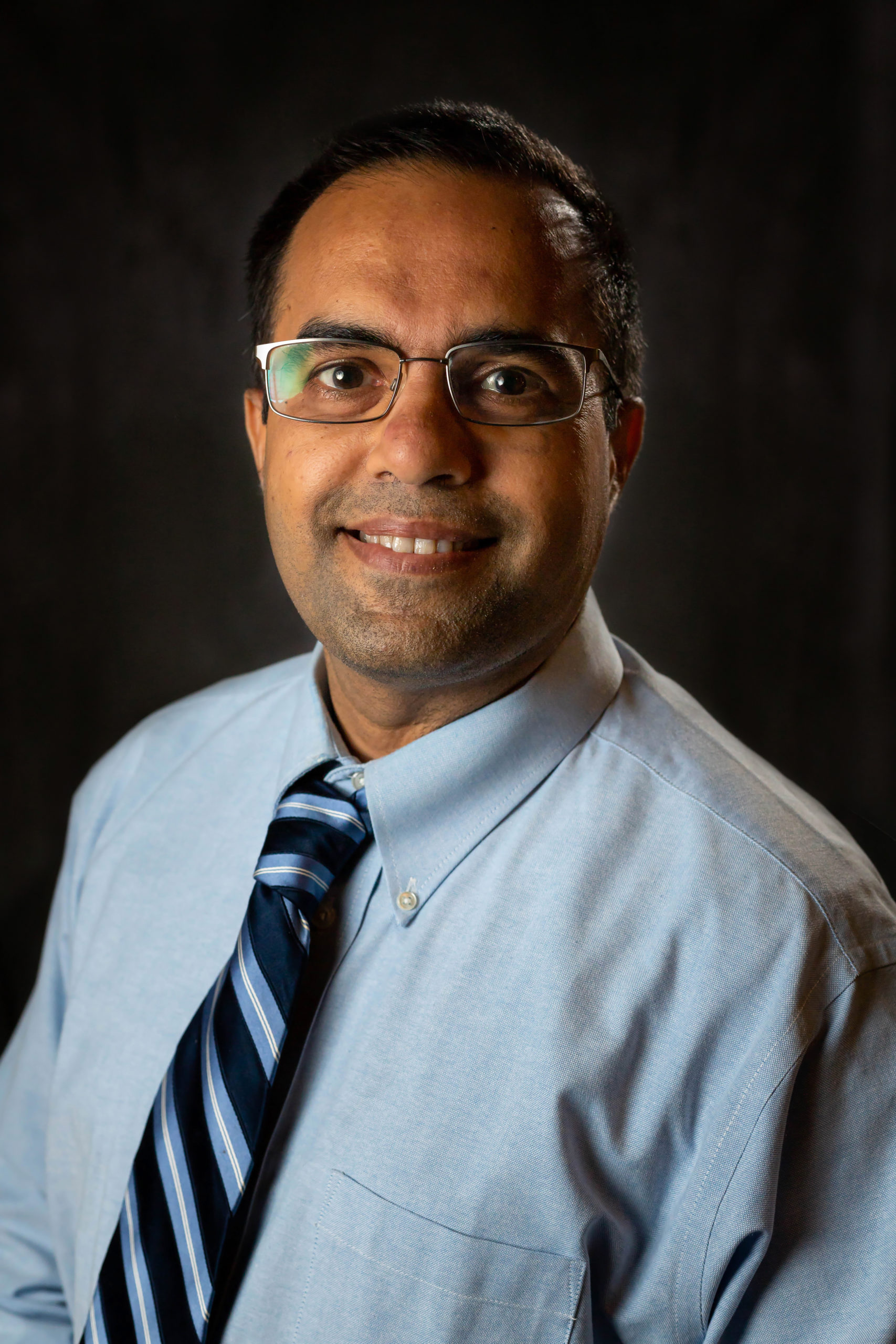 man in light blue shirt and dark blue tie against black background
